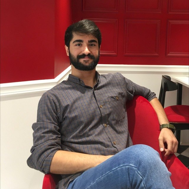 Armin, bearded and smiling, sitting on a red armchair in front of a red panelled wall