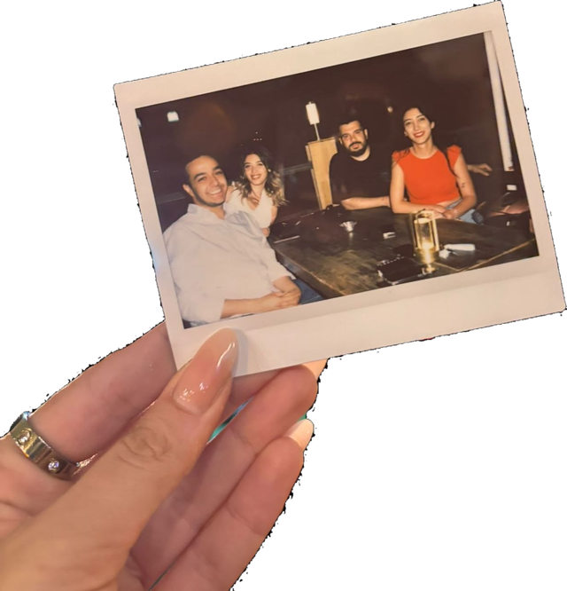 A hand holding a polaroid of four friends smiling around a table at night