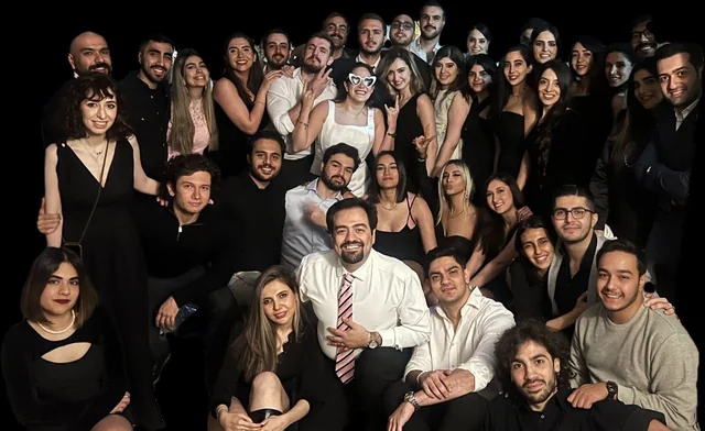 A big group of friends dressed up at a party at night, one in white wearing heart-shaped sunglasses