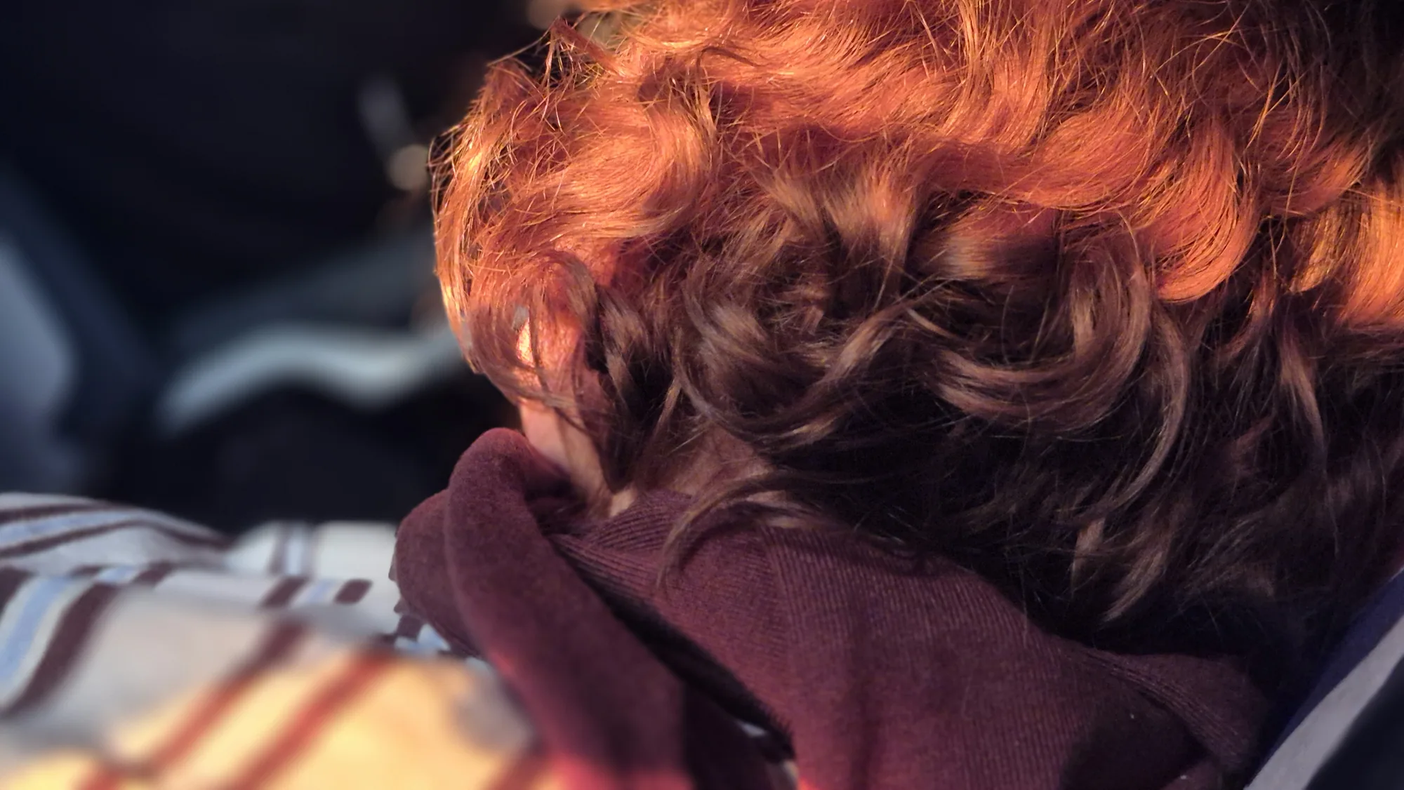 Red curly hair and a maroon hoodie, someone resting their head, seen from behind
