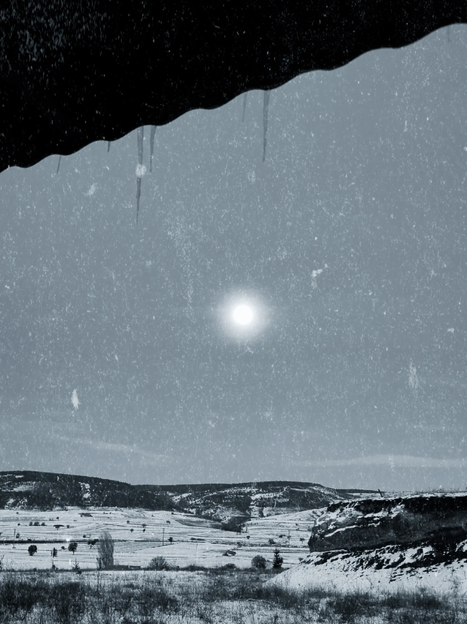 Snowy hills under a pale sun, seen from under a roof edge with icicles