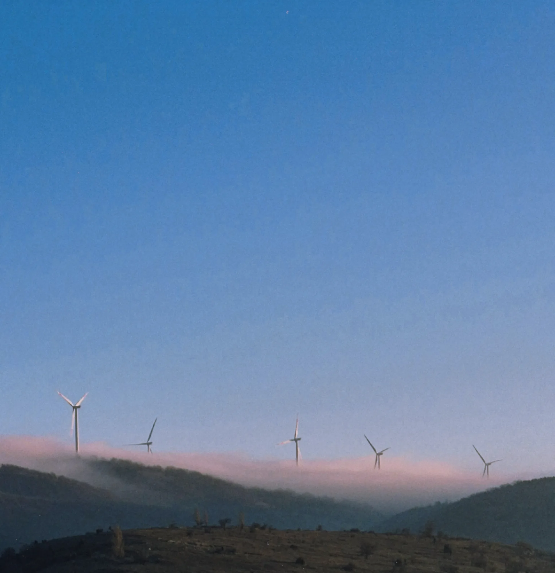 Wind turbines on a ridge above a band of low fog at dusk