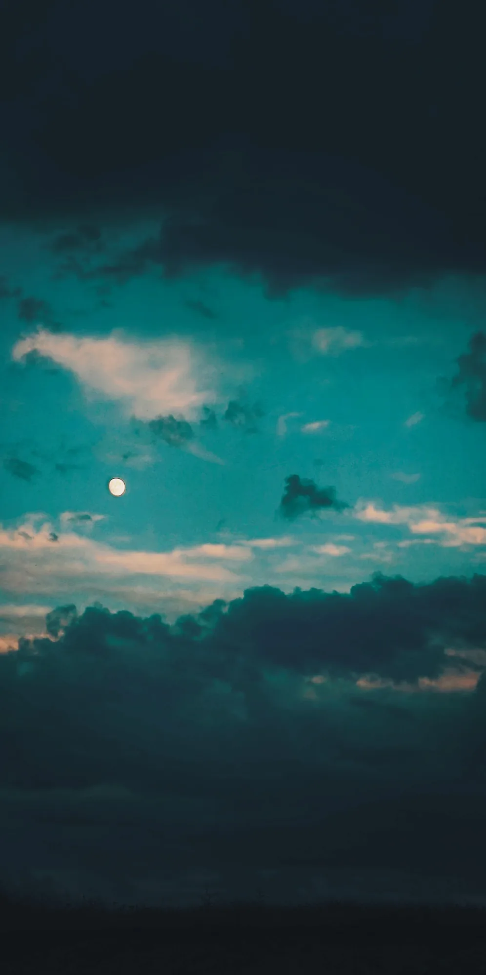 A dark teal sky with heavy clouds and a small moon