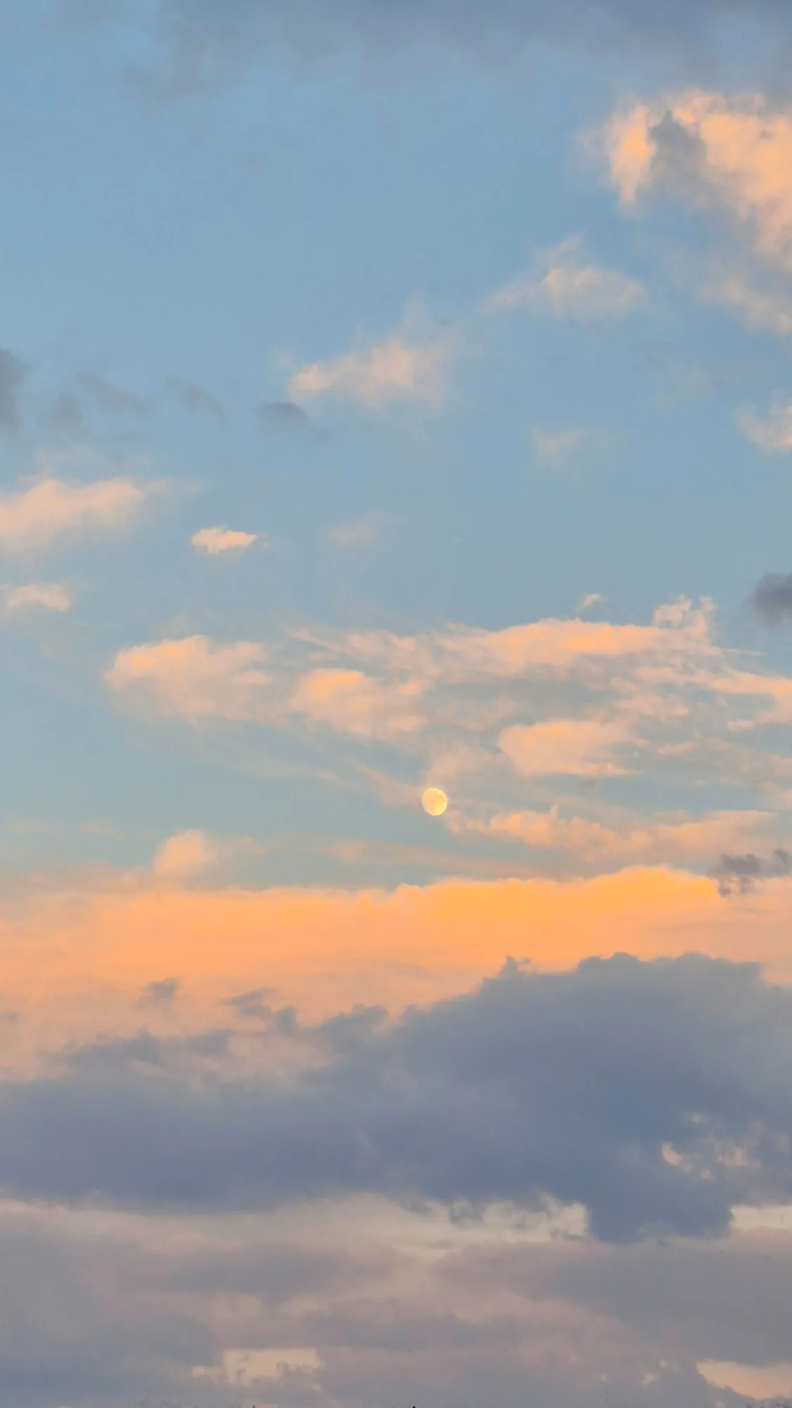 A pale moon among soft orange and pink clouds at dusk