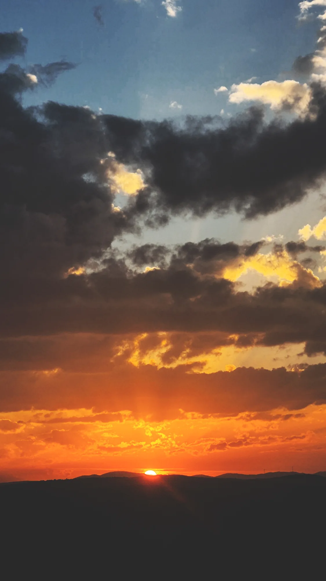 The sun setting behind a ridge under dramatic dark clouds