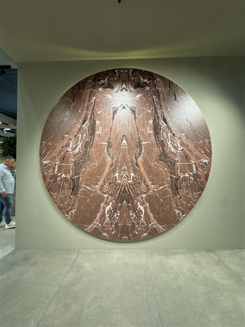 A large round slab with red-brown marble veining, mirrored like a book, on a pale green wall